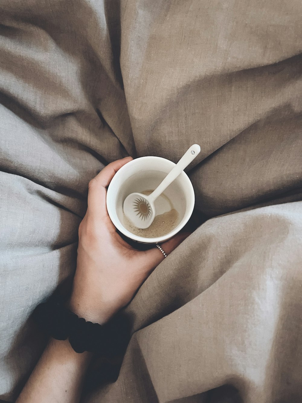 a person holding a cup of coffee on top of a bed