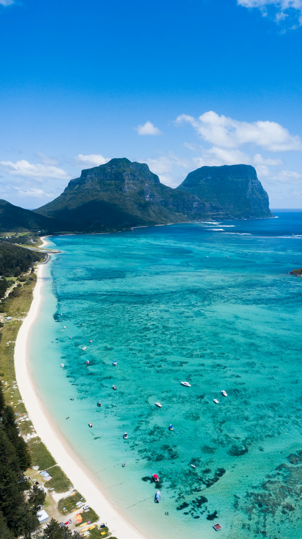 an aerial view of a beach with boats and mountains in the background