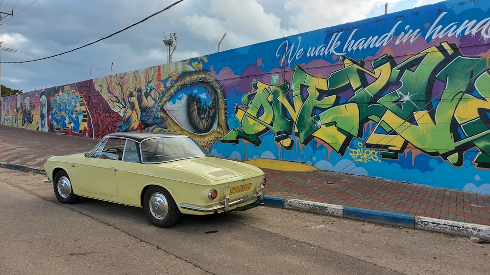 a yellow car parked in front of a colorful wall