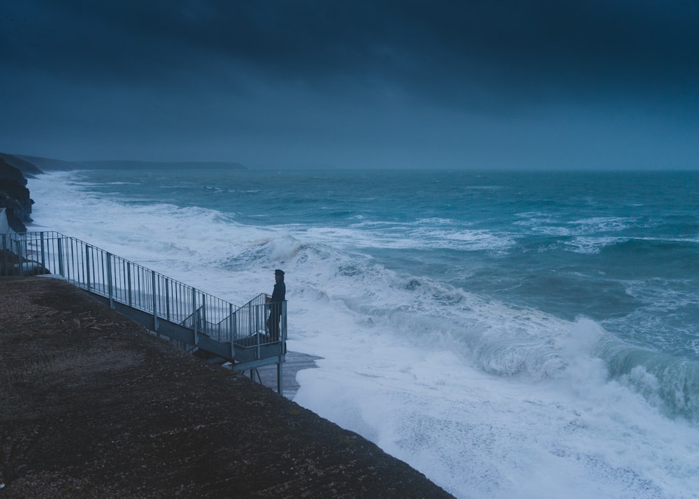 a person standing on a railing next to the ocean