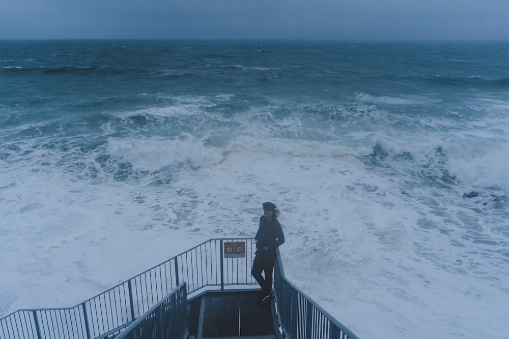 a person standing on a railing near the ocean