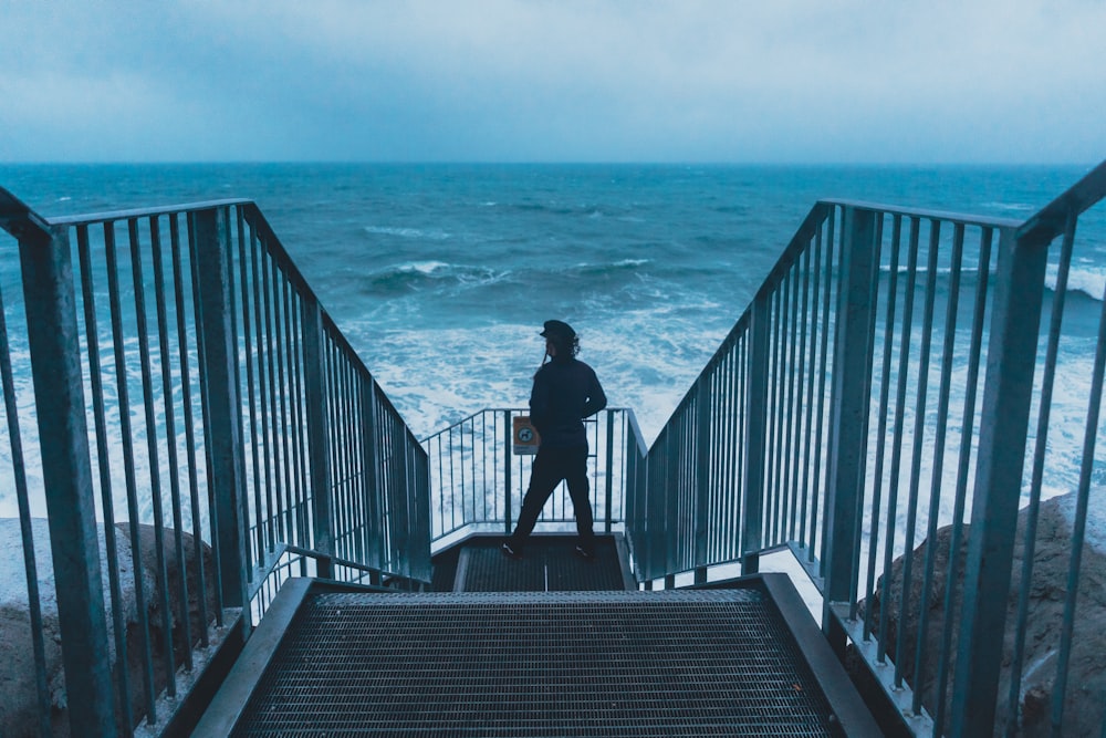 a person standing at the top of a stairway near the ocean