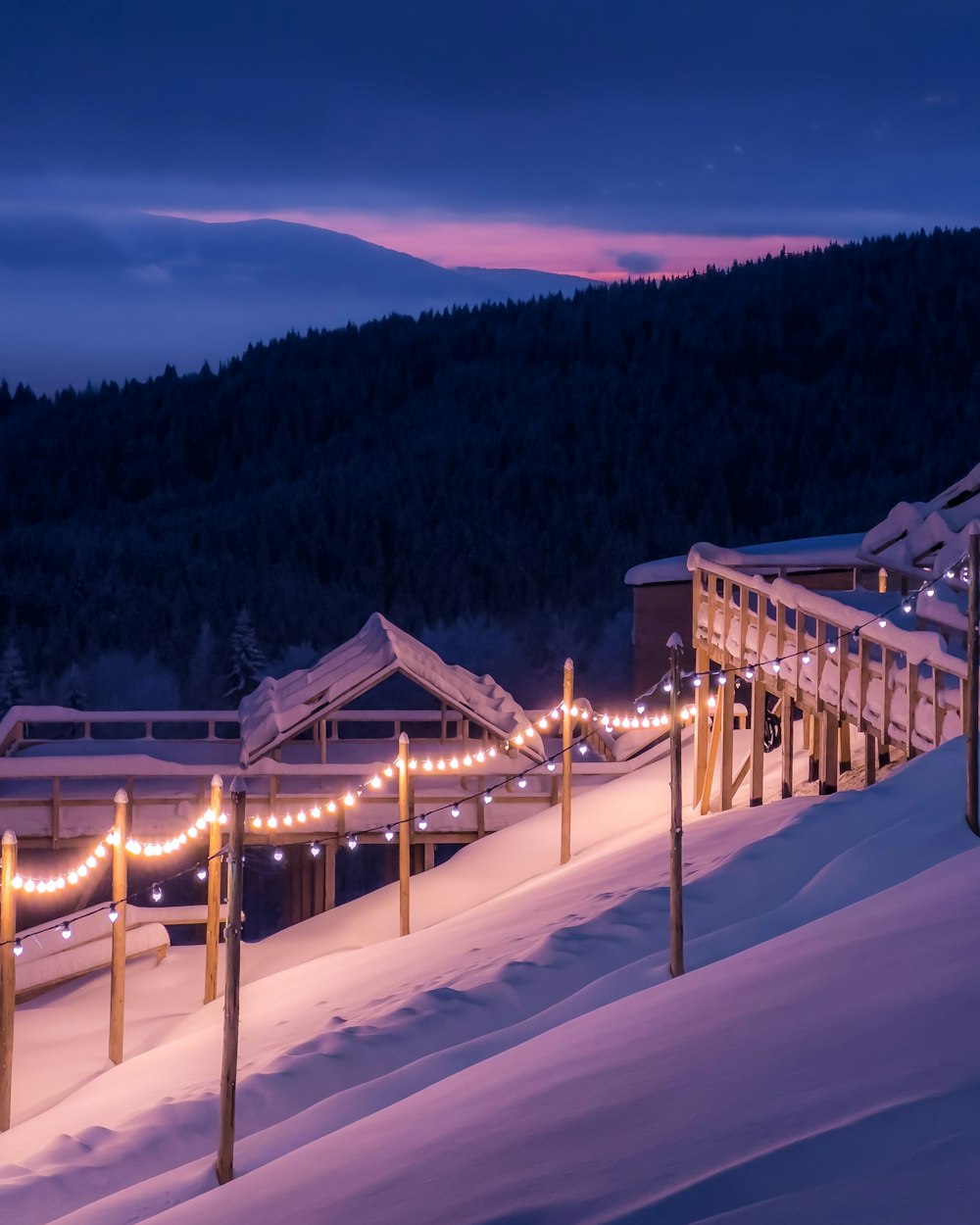 a snowy hill with a bridge and lights on it