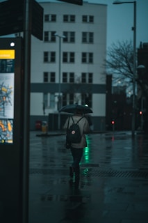 A commuter wearing the backpack walking through a city street on a rainy day