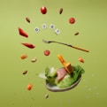 Floating food items including cherry tomatoes, almonds, cashews, slices of red bell pepper, cheese cubes, lettuce, and ham. A fork is levitating among these ingredients. The letters spelling 'DIET' are arranged with small tiles like a game. The background is a solid light green color.