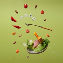 Floating food items including cherry tomatoes, almonds, cashews, slices of red bell pepper, cheese cubes, lettuce, and ham. A fork is levitating among these ingredients. The letters spelling 'DIET' are arranged with small tiles like a game. The background is a solid light green color.