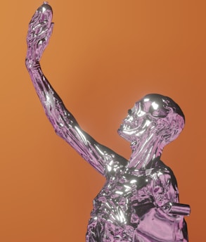 A reflective, metallic humanoid figure crafted in a skeletal form with an arm raised high, standing against a warm orange background. The figure seems to be gazing at or holding something in its hand, exhibiting a sense of contemplation.