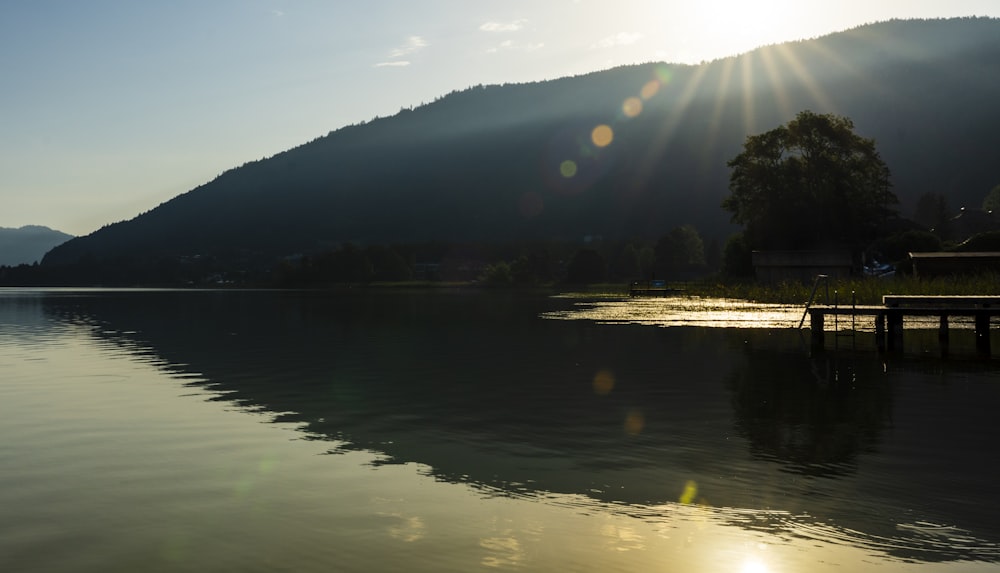 the sun is shining over a lake with a dock