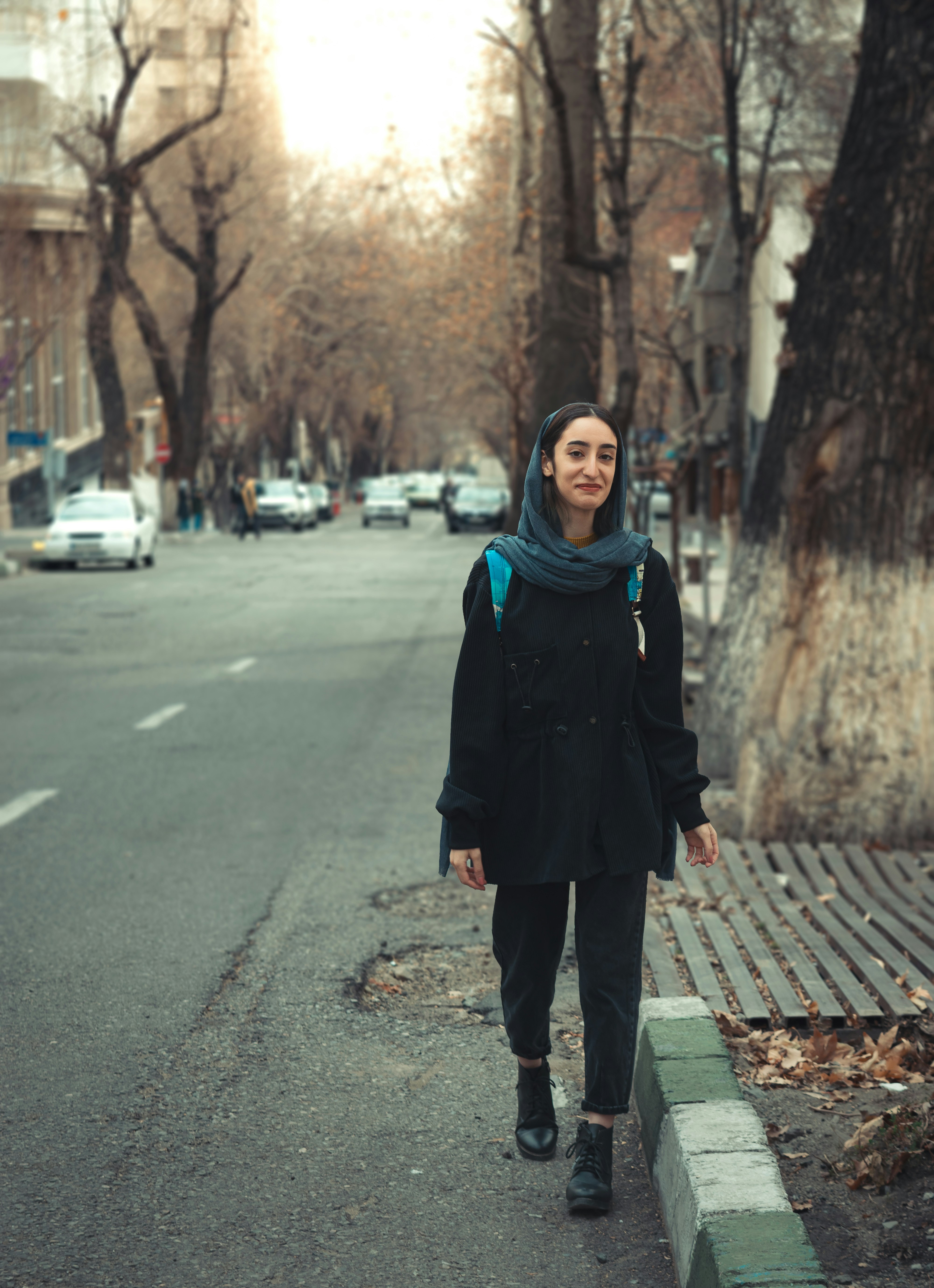 a woman walking down a street next to a tree