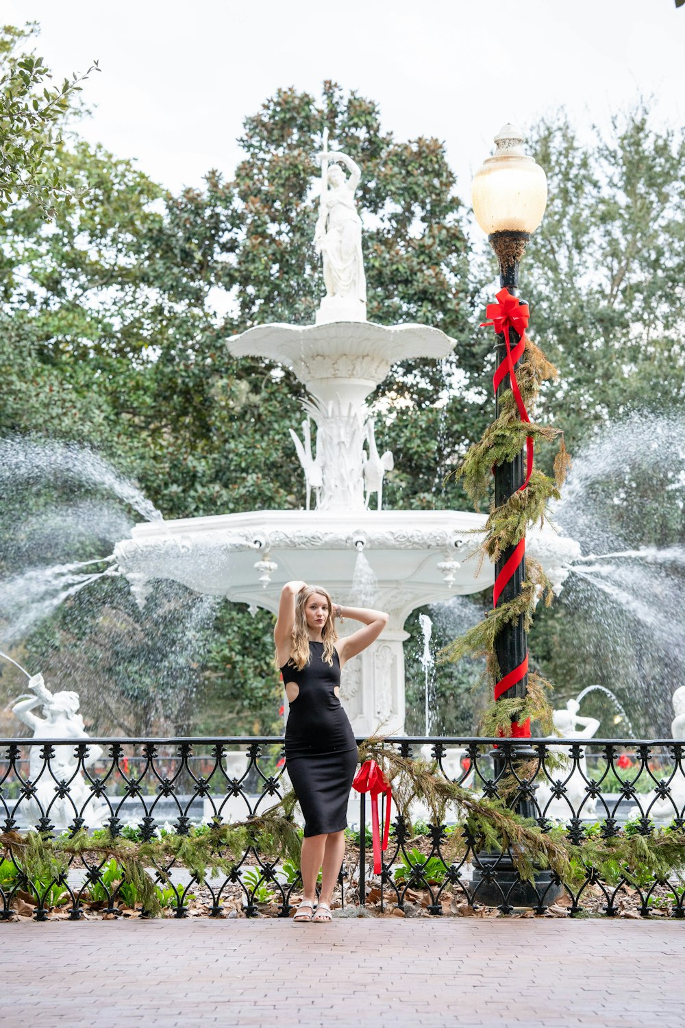 a woman in a black dress standing in front of a fountain