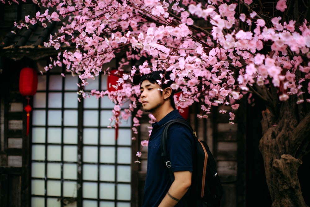 Un hombre parado debajo de un árbol con flores rosadas