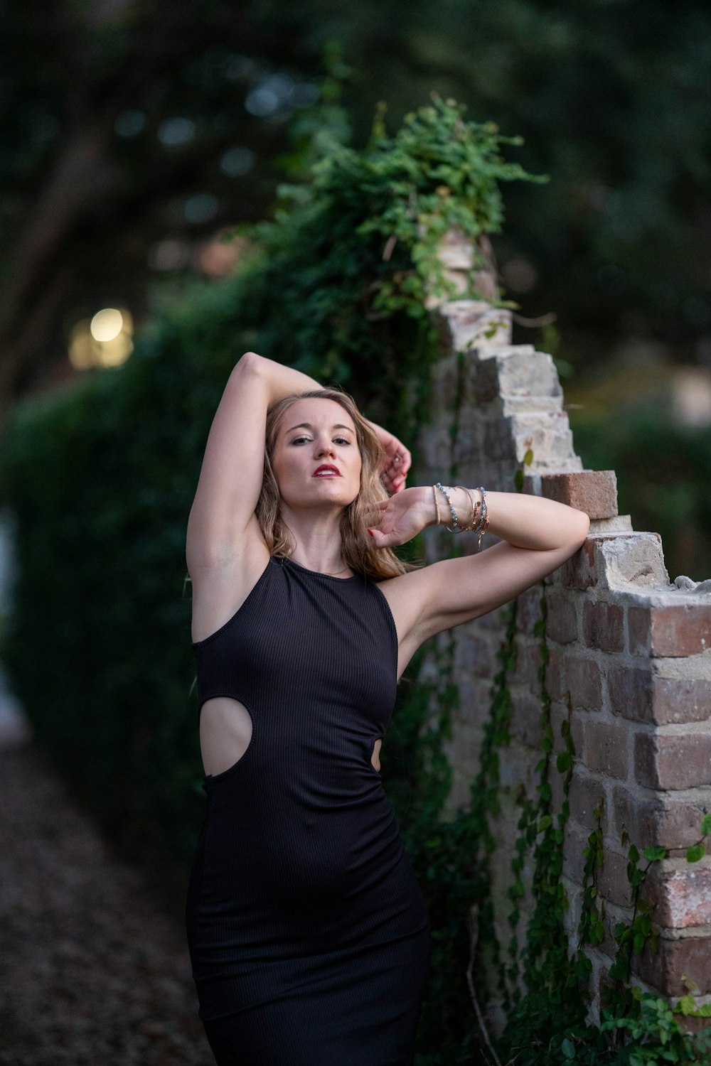 a woman in a black dress leaning against a brick wall
