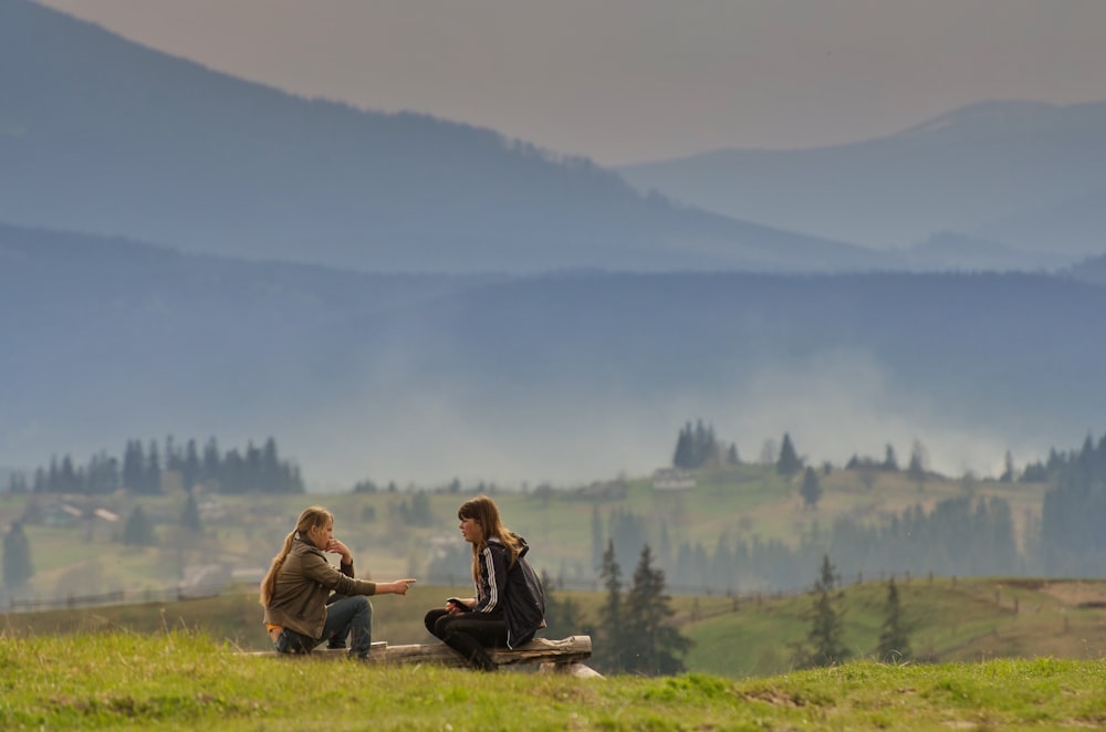 a couple of women sitting on top of a lush green hillside