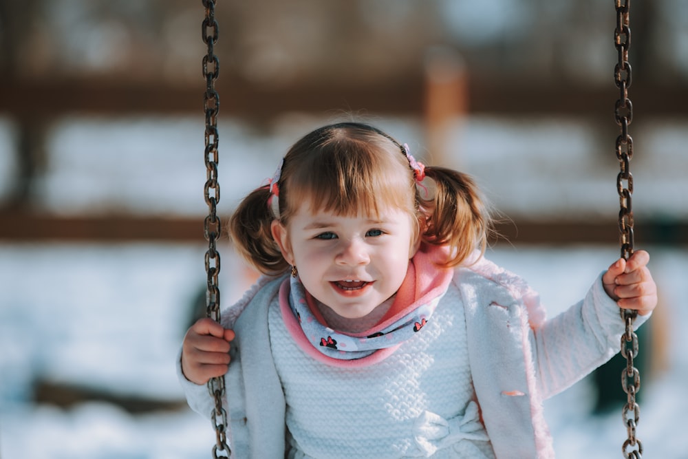 a little girl sitting on a swing in the snow