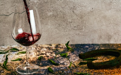 A glass of wine is being poured with a background featuring a rustic table scattered with green leaves and a rusted horseshoe. The scene conveys a sense of rustic charm and casual elegance.