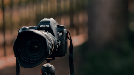 a canon camera attached to a tripod in front of a fence