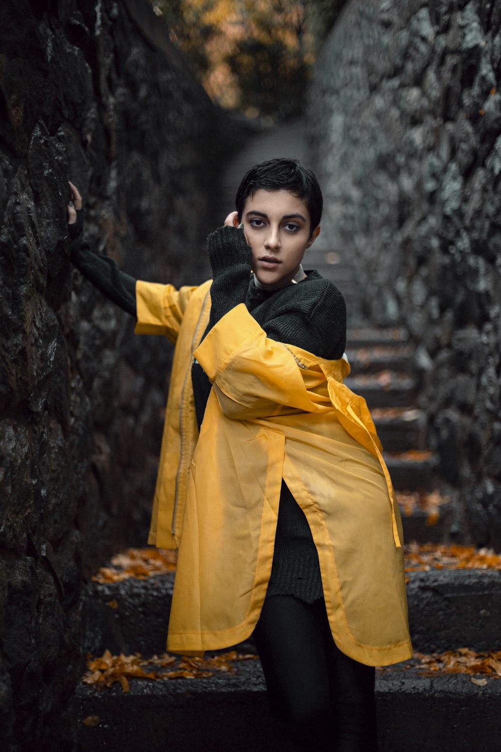 a woman in a yellow raincoat leaning against a stone wall