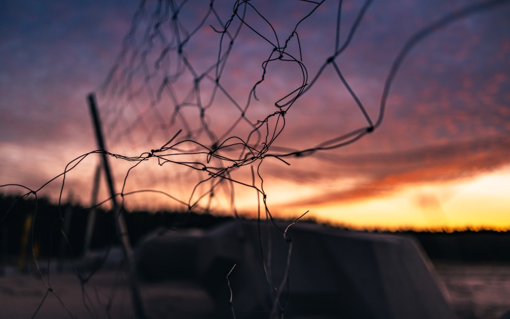 a close up of a fence with a sunset in the background