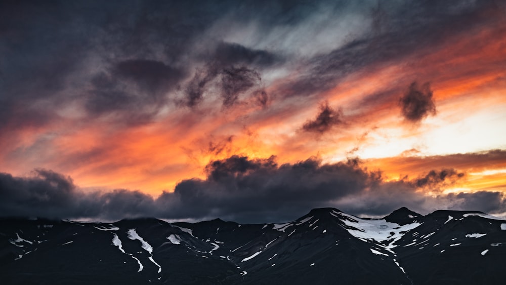 a mountain range covered in snow under a cloudy sky