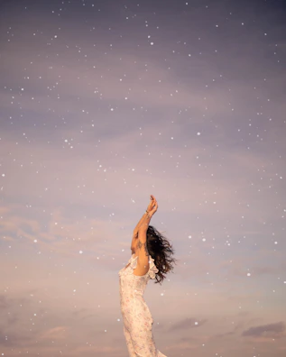 a woman in a white dress reaching up into the sky