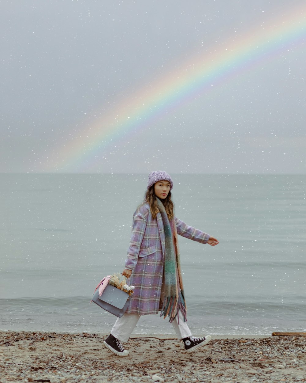 a woman walking on a beach with a rainbow in the background