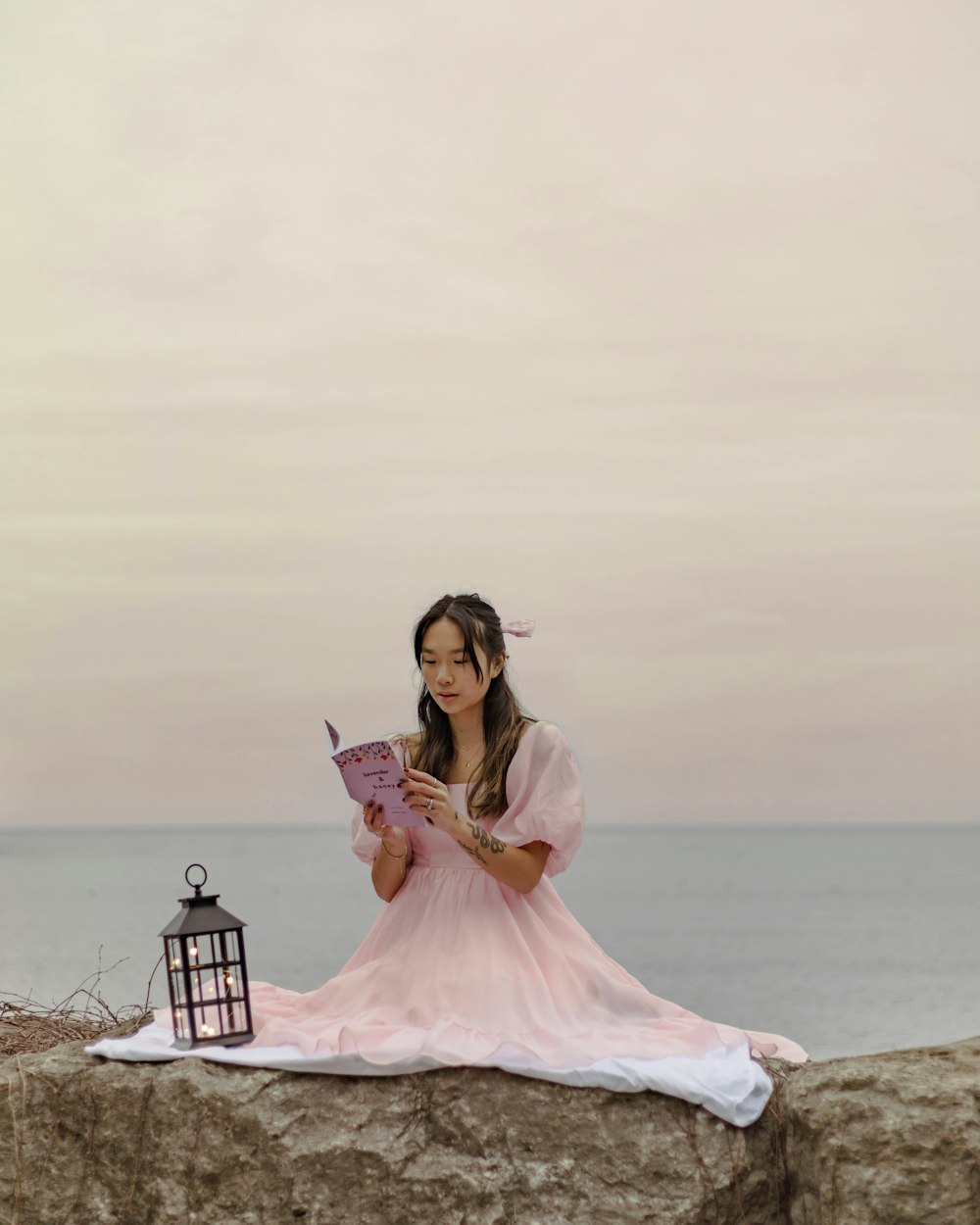 a woman in a pink dress sitting on a rock next to a lantern