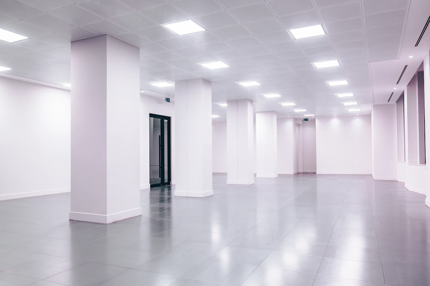 Bright vacant commercial interior with white walls, columns and tiled flooring.