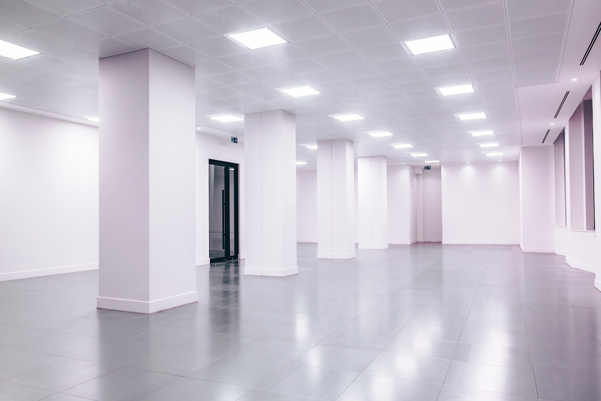 A modern open-plan commercial office space mid fit-out, with newly installed suspended ceiling and lighting, freshly painted white walls and structural columns, and a finished floor awaiting furniture and partitions.