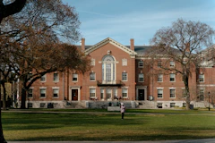 A red-brick college building behind a lawn and autumn trees