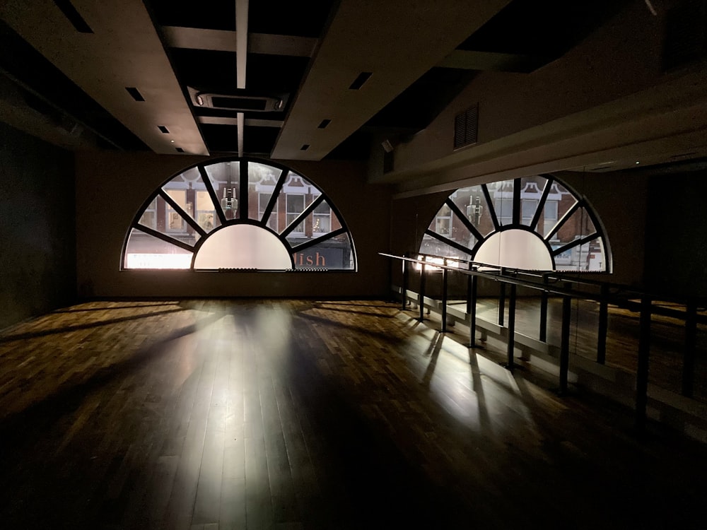 a dark room with large arched windows and wooden floors