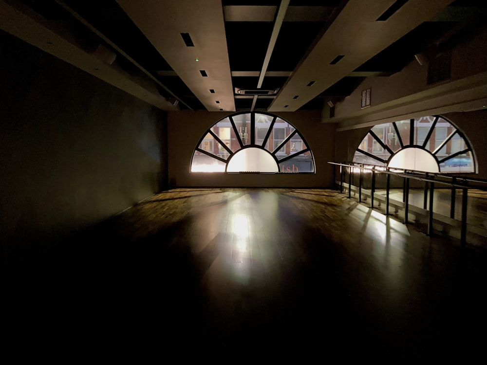 a dark room with large arched windows and a wooden floor