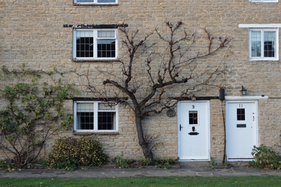 a brick building with two white doors and a tree in front of it
