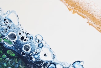 An abstract design featuring a mix of organic shapes reminiscent of cells or bubbles. On the left, hues of blue and green intermingle, creating a textured appearance. To the right, a warm orange border contrasts against a stark white background.
