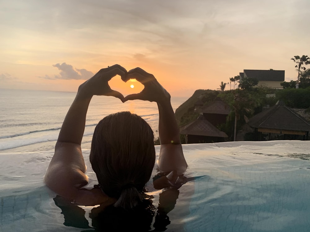 a woman sitting in a pool making a heart with her hands