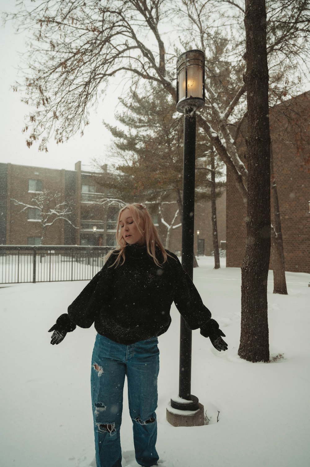 a woman standing in the snow next to a lamp post
