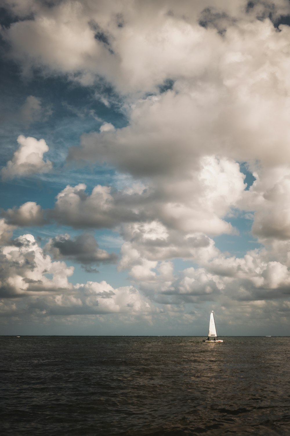 a sailboat in the middle of the ocean under a cloudy sky