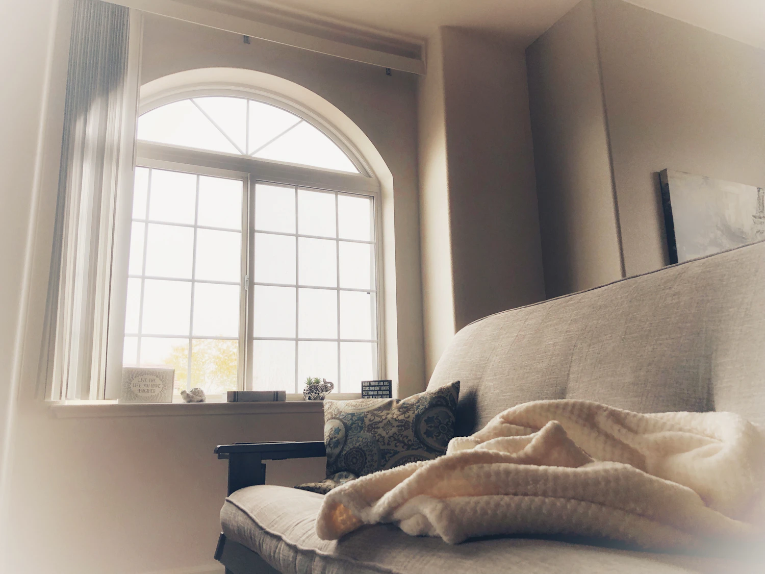 A linen-covered sofa under a tall window with the blind half drawn