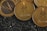 Several cryptocurrency coins, prominently displaying the Ethereum symbol and name, rest closely together. The background features a textured, black granular surface, creating a contrasting backdrop for the shiny, gold-colored coins.