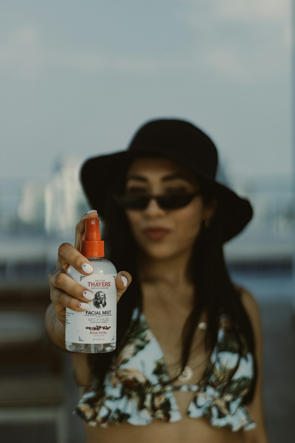 a woman in a hat and sunglasses holding a bottle of sunscreen