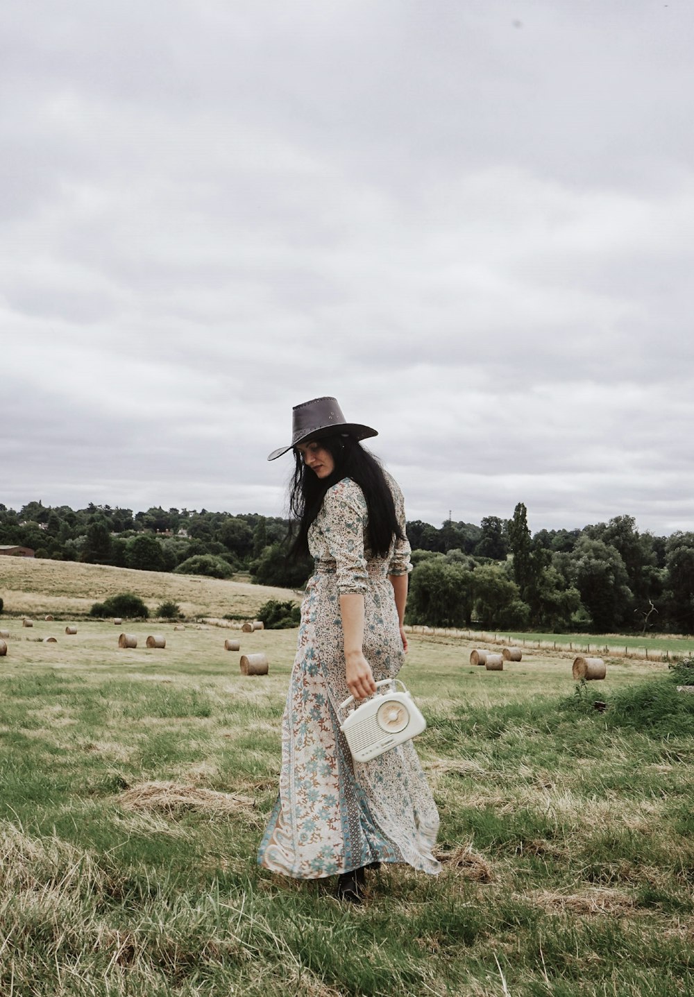 a woman in a dress and hat walking in a field