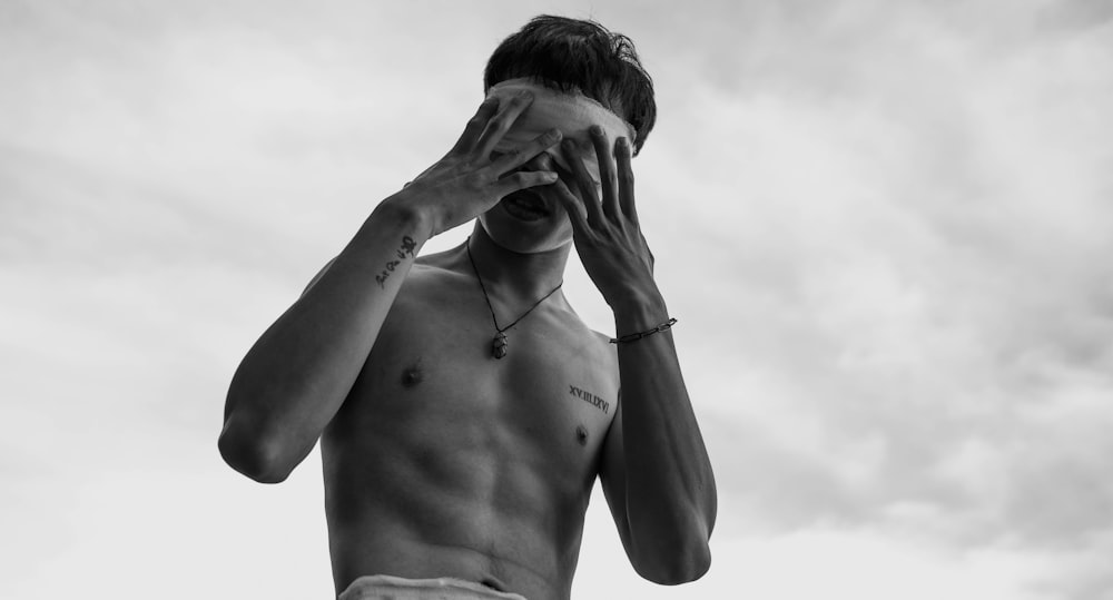 a shirtless man covers his face with his hands