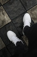 a person standing on a tile floor wearing white sneakers