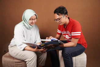 a man and a woman sitting on a bench looking at a book