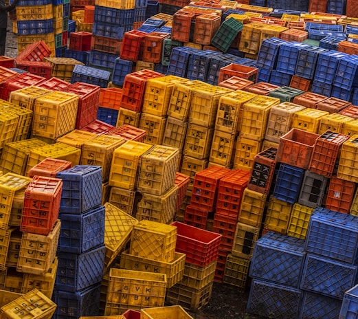 Plastic crates stacked outdoors under bright sunlight, showing their sturdy build.