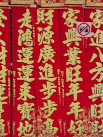 Bright red vertical banners display large gold Chinese characters with intricate decorative patterns. A small no-photography sign is partially visible, featuring a crossed-out camera icon.