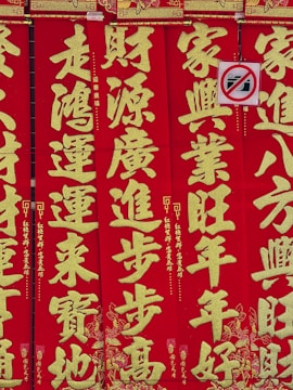 Bright red vertical banners display large gold Chinese characters with intricate decorative patterns. A small no-photography sign is partially visible, featuring a crossed-out camera icon.
