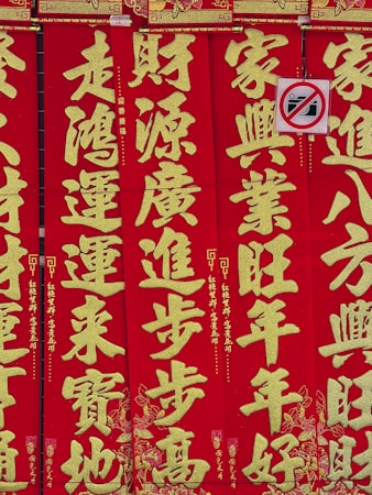 Bright red vertical banners display large gold Chinese characters with intricate decorative patterns. A small no-photography sign is partially visible, featuring a crossed-out camera icon.
