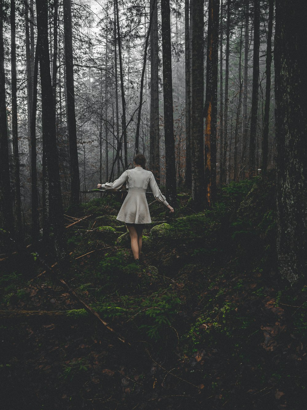 a woman in a white dress walking through a forest