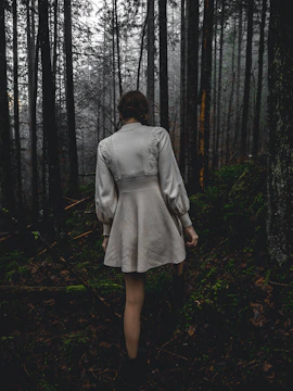 A giant alien woman in a shimmering dress walking through a foggy forest.