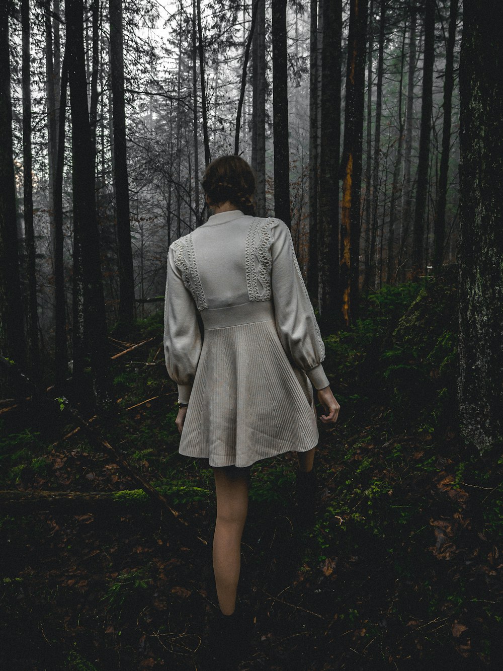 a woman in a white dress walking through a forest